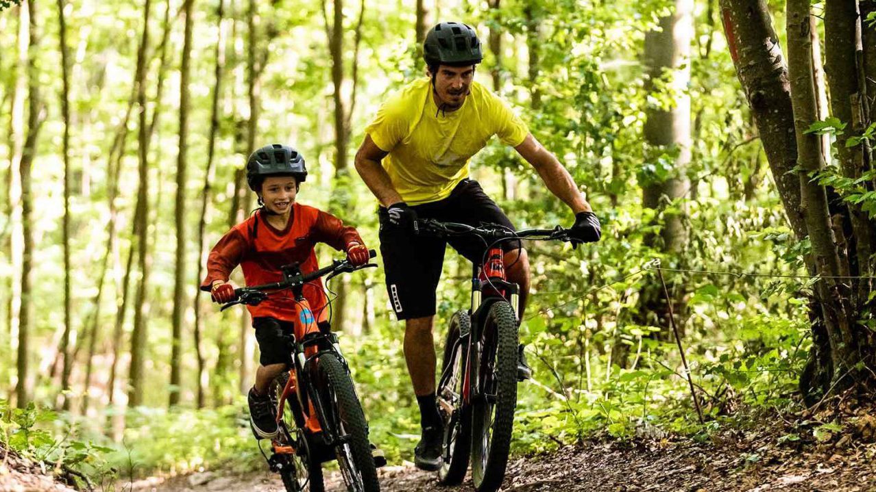 Părinte și copil pedalând împreună prin pădure